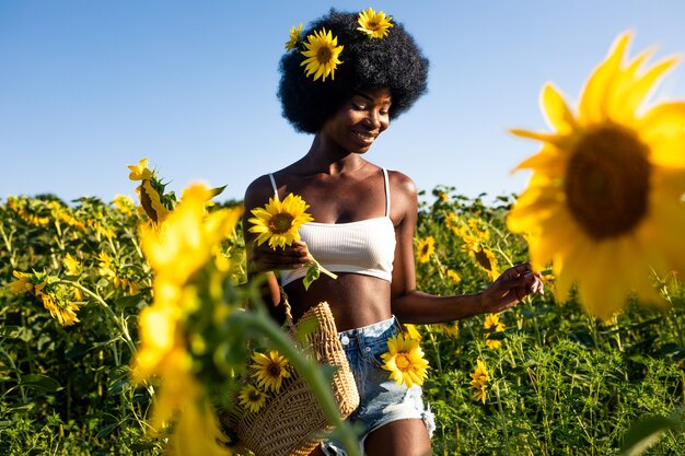 Mooie afro-amerikaanse vrouw met krullend haar in afrostijl in een zonnebloemenveld