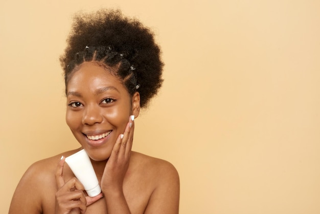 Foto mooie afro-amerikaanse vrouw met vochtinbrengende crème of masker op beige achtergrond met kopieerruimte huidverzorging tegen veroudering