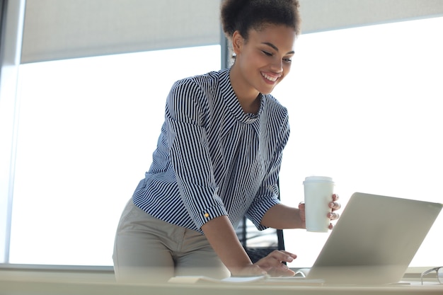 Mooie Afro-Amerikaanse zakenvrouw in slimme vrijetijdskleding die op laptop op kantoor werkt.