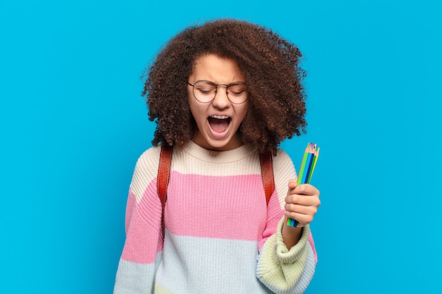 Mooie afro-tiener die agressief schreeuwt, erg boos, gefrustreerd, verontwaardigd of geïrriteerd kijkt en nee schreeuwt. studentenconcept