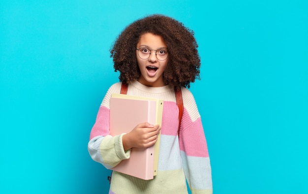 Mooie afro-tiener die erg geschokt of verrast kijkt, starend met open mond en zegt wow.