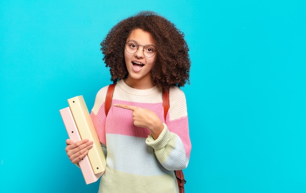 Mooie afro-tiener die opgewonden en verrast kijkt naar de zijkant en naar boven wijst om ruimte te kopiëren