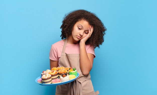 Mooie afro-tiener die zich verveeld, gefrustreerd en slaperig voelt na een vermoeiende, saaie en vervelende taak, gezicht met de hand vasthoudend. humoristisch bakkersconcept