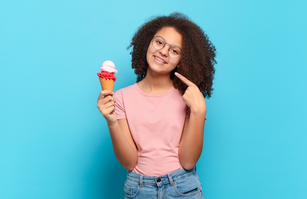 Mooie afro tiener glimlachend vol vertrouwen wijzend naar eigen brede glimlach, positieve, ontspannen, tevreden houding.