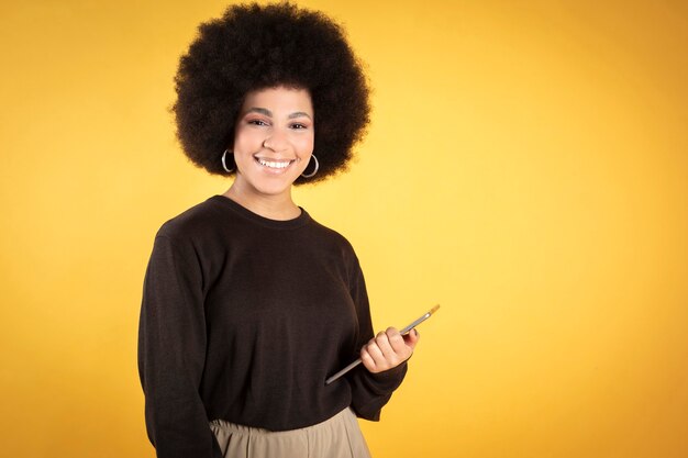 Mooie afro-vrouw die lacht, met haar hand een tablet, technologie, gele achtergrond