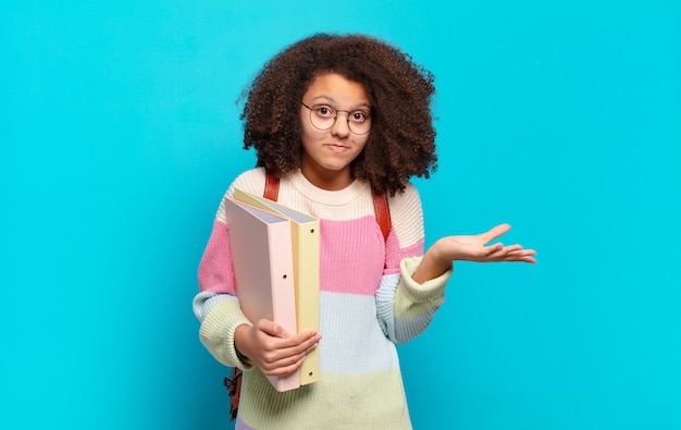 Mooie afro-vrouw die zich verbaasd en verward voelt, twijfelt, weegt of verschillende opties kiest met een grappige uitdrukking. student concept