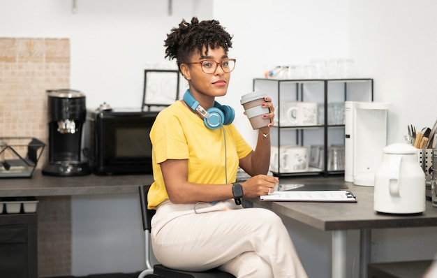 Mooie afro-vrouw met een bril op kantoor die koffie drinkt