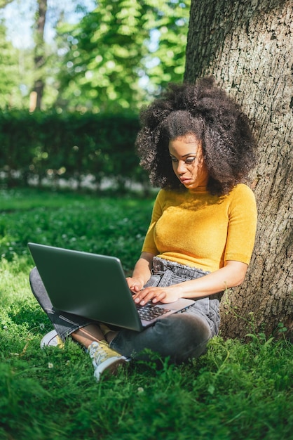 Mooie afrovrouw die op laptop in een tuin typt. Selectieve aandacht.