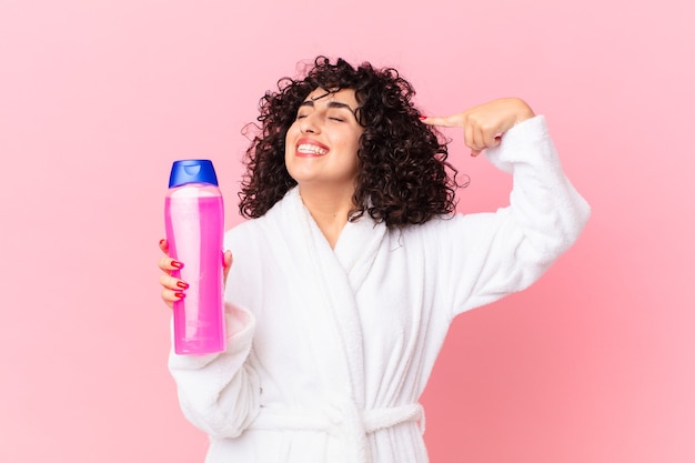 mooie Arabische vrouw die een badjas draagt en een shampoofles vasthoudt