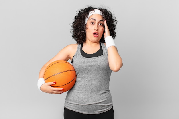 Mooie arabische vrouw die er blij, verbaasd en verrast uitziet en een basketbalbal vasthoudt. sport concept