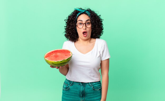 Mooie arabische vrouw die erg geschokt of verrast kijkt en een watermeloen vasthoudt. zomer concept