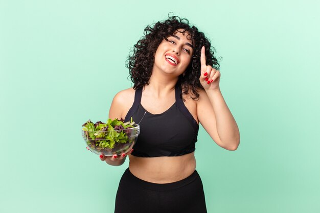 Mooie arabische vrouw die zich een gelukkig en opgewonden genie voelt nadat ze een idee heeft gerealiseerd en een salade vasthoudt. dieet concept