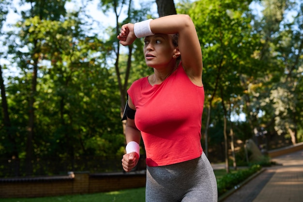 Mooie atleet vrouw runner veegt het zweet van haar gezicht met behulp van badstof polsbandje tijdens het hardlopen in het stadspark haar lichaam fit houden Gezond en actief levensstijl concept