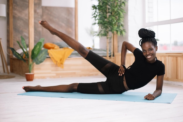 Mooie atletische Afro-Amerikaanse vrouw liggend aan de zijkant en verhogen been selectieve aandacht training op gym mat in ingerichte fotostudio Sport cursus oefening techniek fitness lichaam fit houden