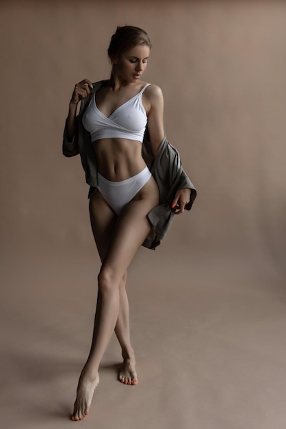 Mooie atletische blanke vrouw in witte lingerie trekt haar shirt uit op een beige achtergrond