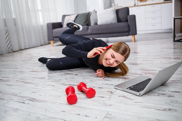 Mooie atletische vrouw in een zwarte top en legging die thuis sport en aan de telefoon praat. Motivatie om te gaan sporten. Gezonde levensstijl.