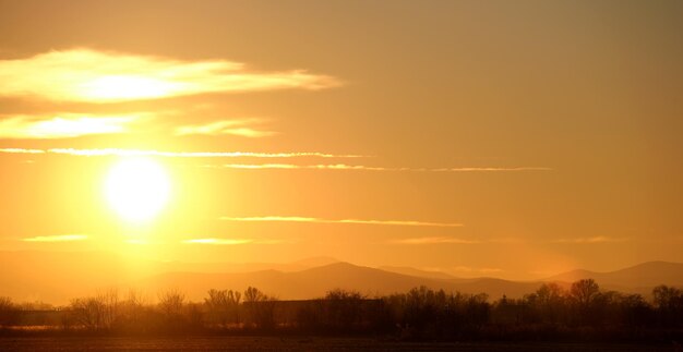 Mooie avond panoramisch landschap met heldere ondergaande zon over verre bergtoppen bij zonsondergang.