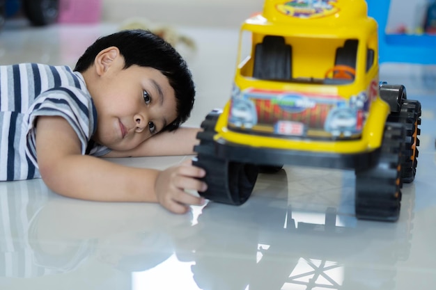 Mooie Aziatische babyjongen spelen met gele speelgoedauto op de vloer thuis