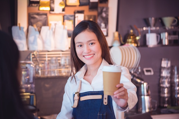 Mooie Aziatische barista die koffiekop geeft aan haar klant en glimlachen in haar koffie