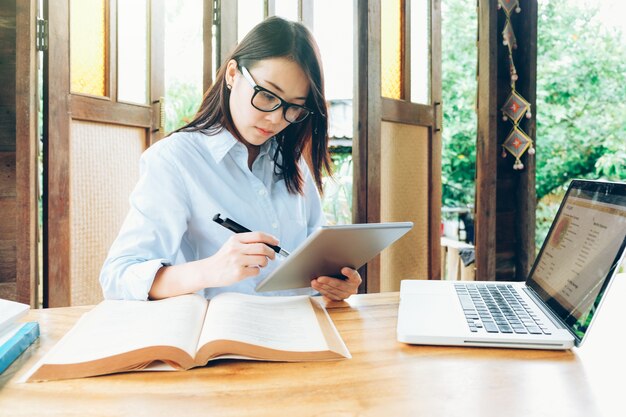 Mooie Aziatische bedrijfsvrouw die met laptop, telefoon, en tablet werkt