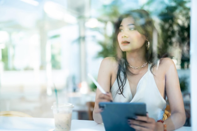 Mooie Aziatische freelance Succes mensen zakenvrouw fashion model in zomer witte mouwloze jurk met behulp van casual werken met tablet voor surfen op internet chatten en bloggen in coffeeshop