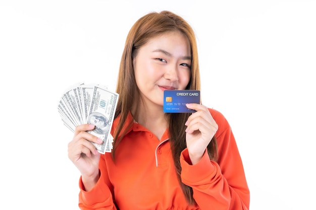 Mooie aziatische jonge vrouw die gelukkig in de ene hand lacht, hield een grote hoeveelheid amerikaanse dollars die ze van haar creditcard had verkregen in haar andere hand - betalend met een online winkelconcept met creditcard