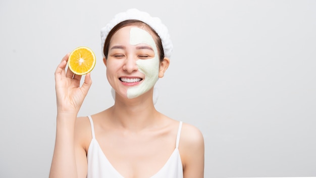 Mooie Aziatische jonge vrouw masker hydraterende en verjongende schone huid peeling terwijl oranje stukjes op een witte achtergrond.