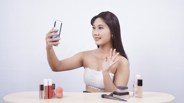 Mooie Aziatische make-up begroet smartphone geïsoleerd op een witte achtergrond