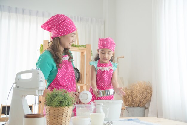 Mooie Aziatische moeder en dochter die roze schort dragen die cake in de keuken maken.