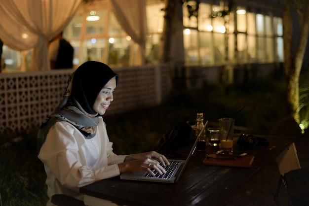 mooie aziatische moslim dame vrijetijdskleding werken met behulp van laptop 's nachts in openluchtcafé