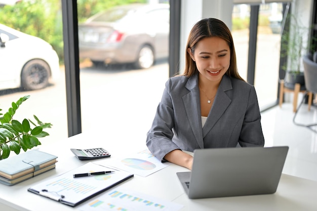 Mooie Aziatische onderneemster die aan financiële en boekhoudkundige taken op laptop werkt