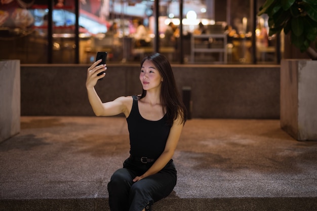 Mooie Aziatische vrouw buitenshuis 's nachts selfie met mobiel te nemen