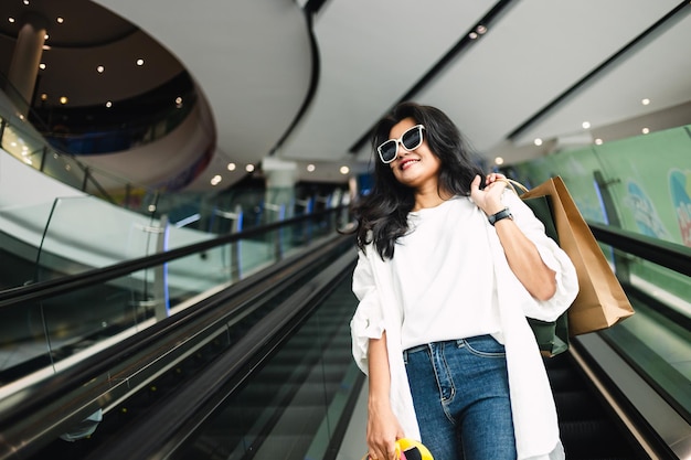 Mooie Aziatische vrouw die boodschappentas vasthoudt en glimlacht tijdens het wandelen in het winkelcentrum