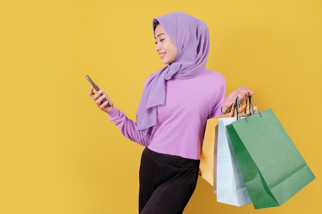 Mooie aziatische vrouw die boodschappentassen toont, die paars t-shirt draagt