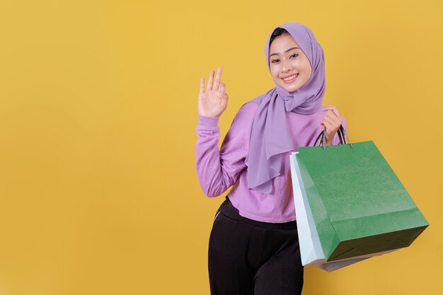 Mooie Aziatische vrouw die boodschappentassen toont, die paars T-shirt draagt