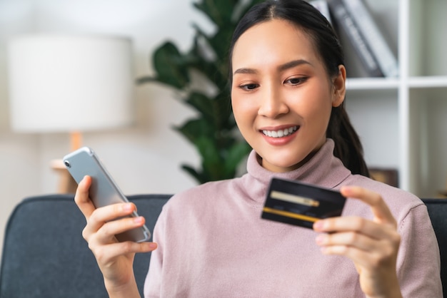 Mooie Aziatische vrouw die creditcard vasthoudt en smartphone gebruikt om online te winkelen met betaling op internetbankieren.