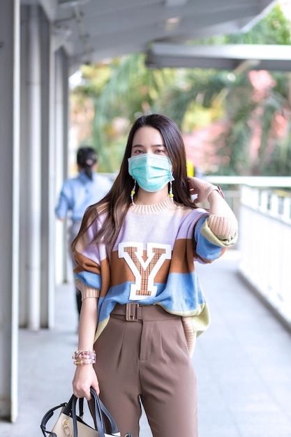 Mooie aziatische vrouw die door de stad loopt, draagt kleurrijke truien, lang haar en medische maskers