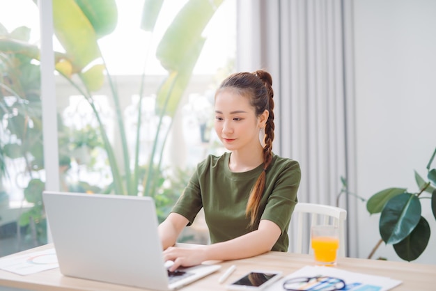 Mooie Aziatische vrouw die e-mail typt op een laptop terwijl ze thuis zit