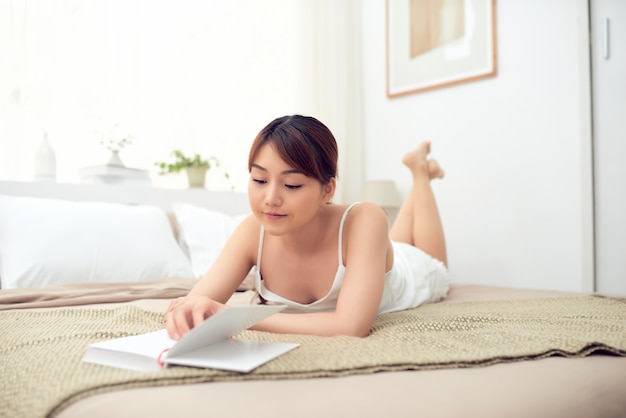 Mooie Aziatische vrouw die een boek leest en 's ochtends op bed ligt