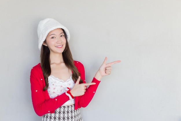 Mooie Aziatische vrouw die een rode jas en een witte hoed draagt als een Santy-meisje doet haar hand om te presenteren