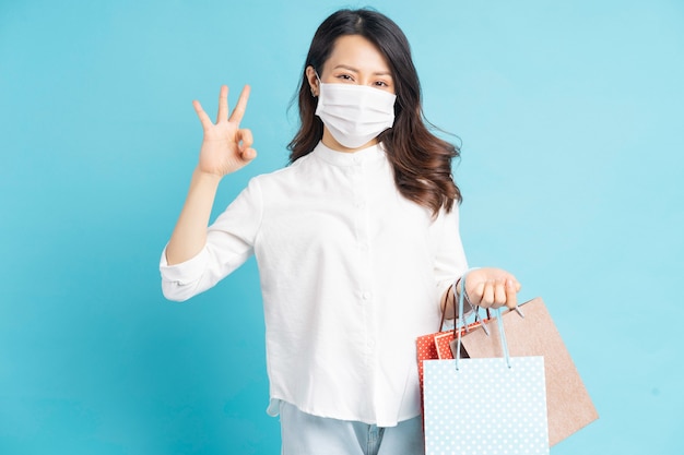 Mooie Aziatische vrouw die een wit masker draagt dat een boodschappentas draagt en met de hand ok maakt