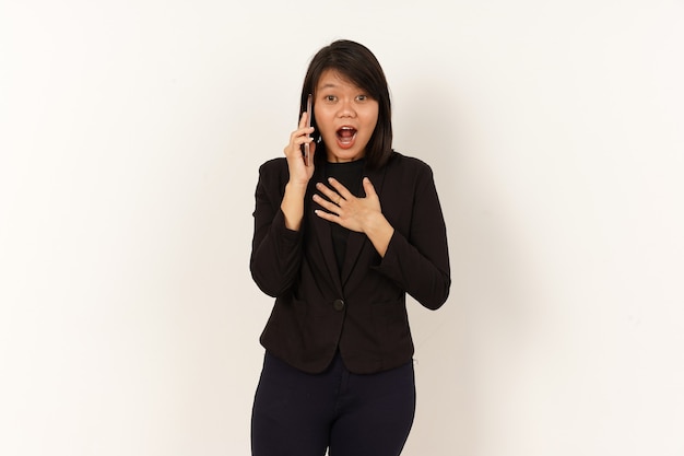 Mooie Aziatische vrouw die een zwart pak draagt en op mobiele telefoon praat met een schokgelaatsuitdrukking
