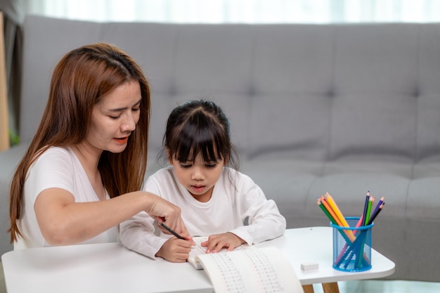 Mooie Aziatische vrouw die haar dochter helpt met huiswerk thuis.