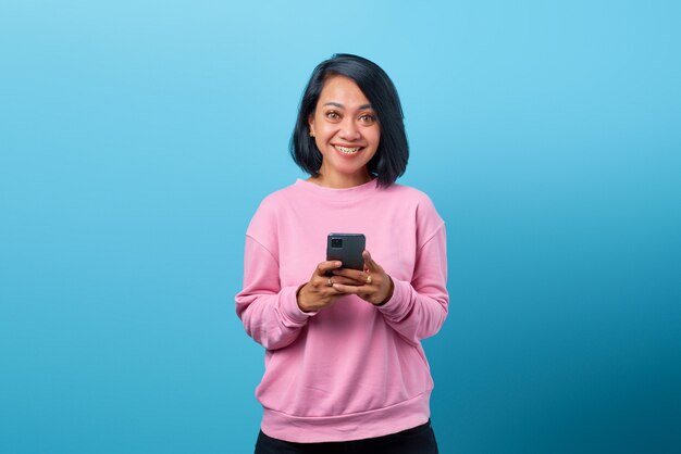 Mooie Aziatische vrouw die lacht met behulp van mobiele telefoon op blauwe achtergrond