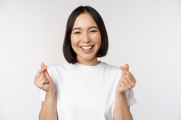 Mooie aziatische vrouw die lacht met een gebaar van vingerharten die een t-shirt draagt dat tegen een witte achtergrond staat