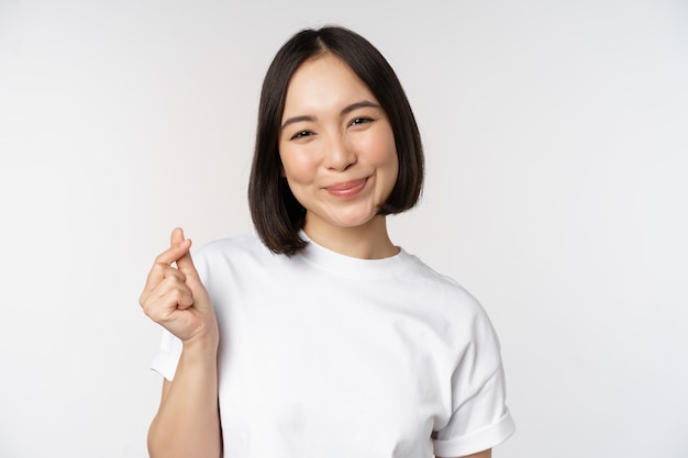 Mooie aziatische vrouw die lacht met een gebaar van vingerharten die een t-shirt draagt dat tegen een witte achtergrond staat