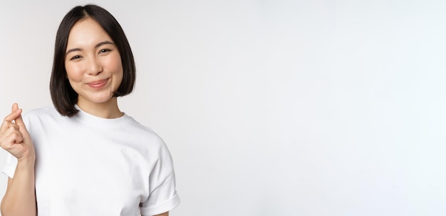 Mooie aziatische vrouw die lacht met een gebaar van vingerharten die een t-shirt draagt dat tegen een witte achtergrond staat