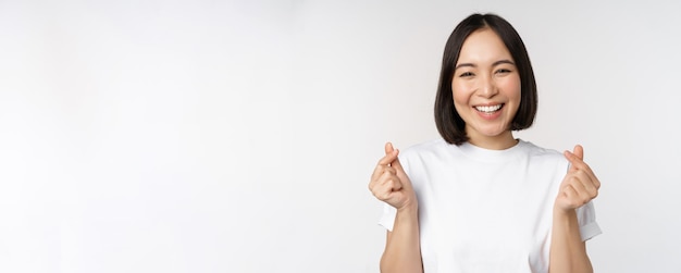 Mooie aziatische vrouw die lacht met een gebaar van vingerharten die een t-shirt draagt dat tegen een witte achtergrond staat