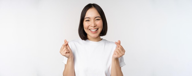 Mooie aziatische vrouw die lacht met een gebaar van vingerharten die een t-shirt draagt dat tegen een witte achtergrond staat