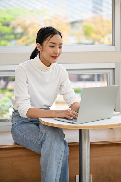Mooie Aziatische vrouw die laptop gebruikt die haar project op afstand beheert in een coworking-ruimte